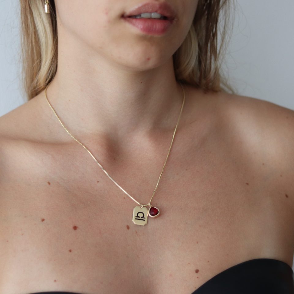 A necklace for a woman in gold color with a zodiac pendant in the shape of a rectangle and stone
