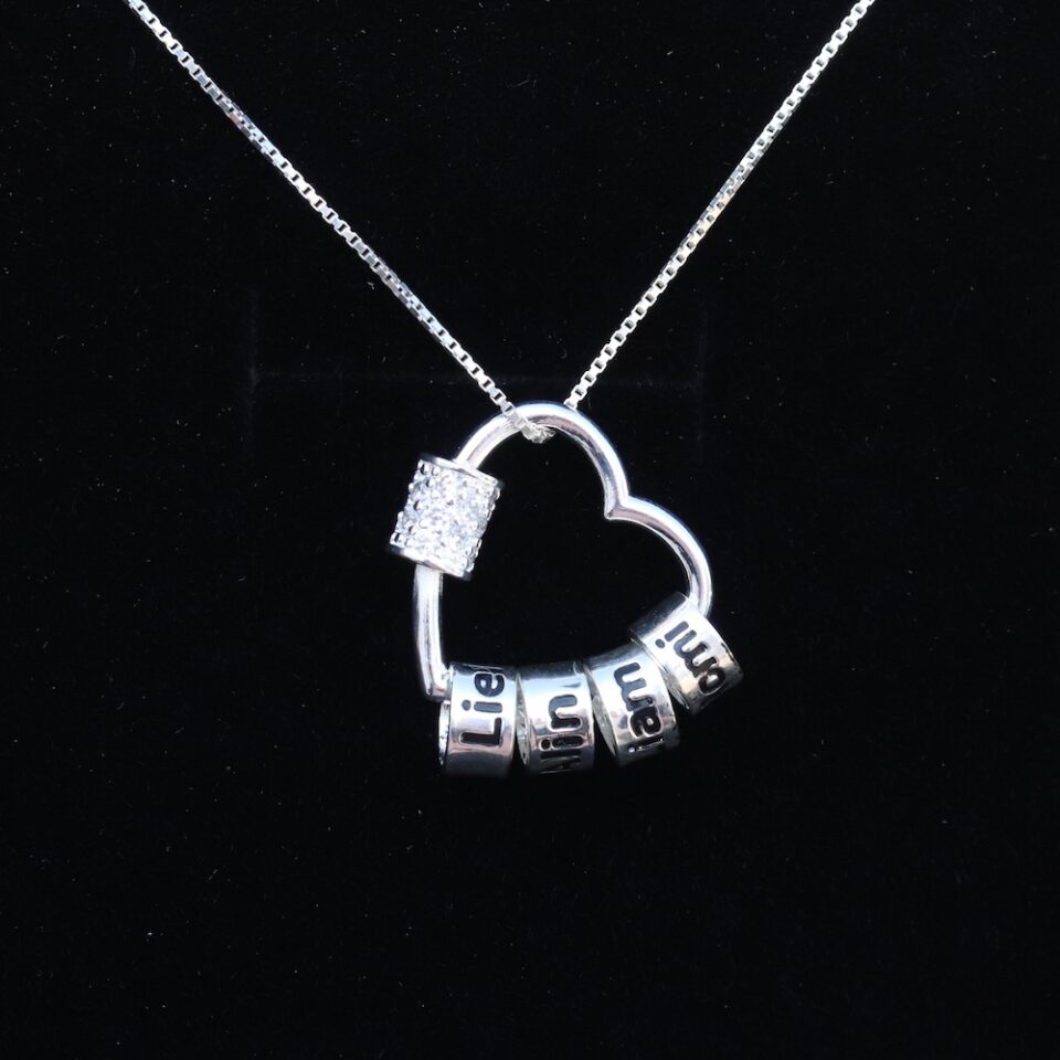 A silver necklace with a heart pendant and inside it engraved beads with the children's names